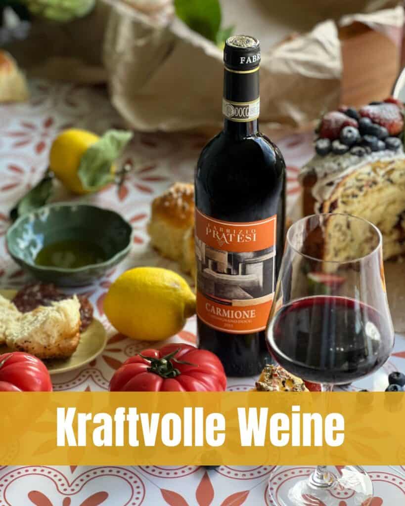 Flasche Carmione Toscana DOCG Rotwein mit Glas Wein, Tomaten, Brot, Zitronen und Kuchen auf dekorativem Tisch.