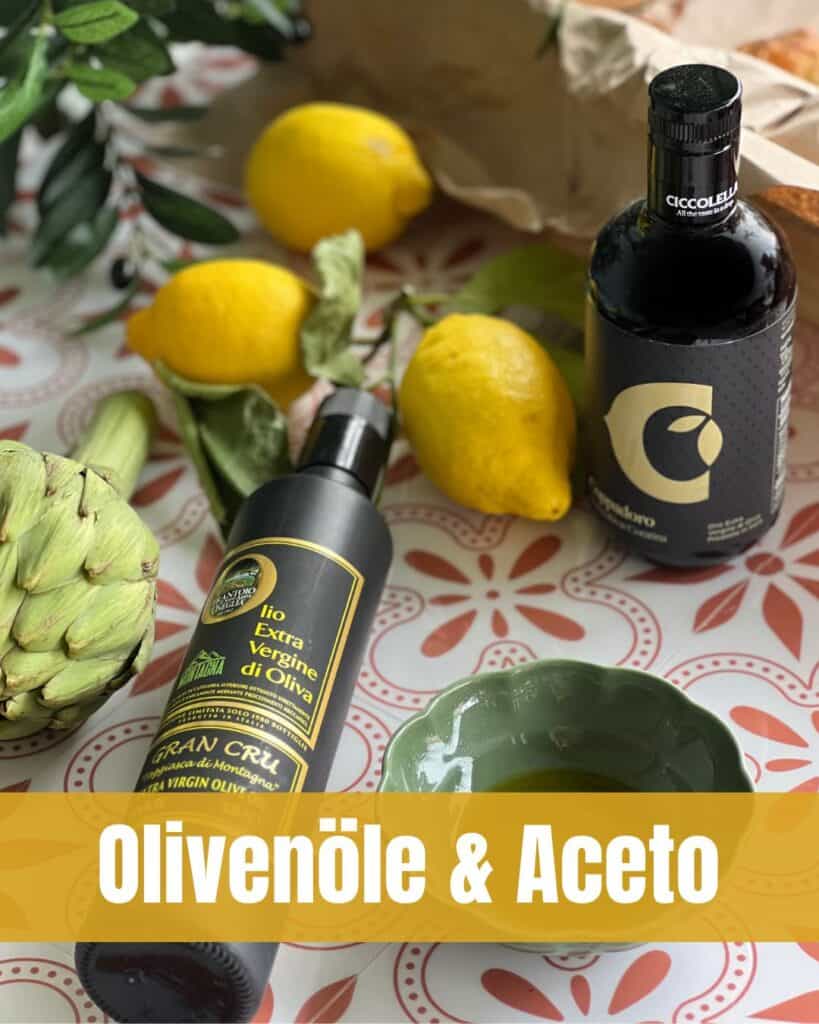 Flaschen mit hochwertigem Olivenöl und Aceto, umgeben von Zitronen, Artischocke, Brot und Olivenzweigen auf mediterranem Hintergrund.