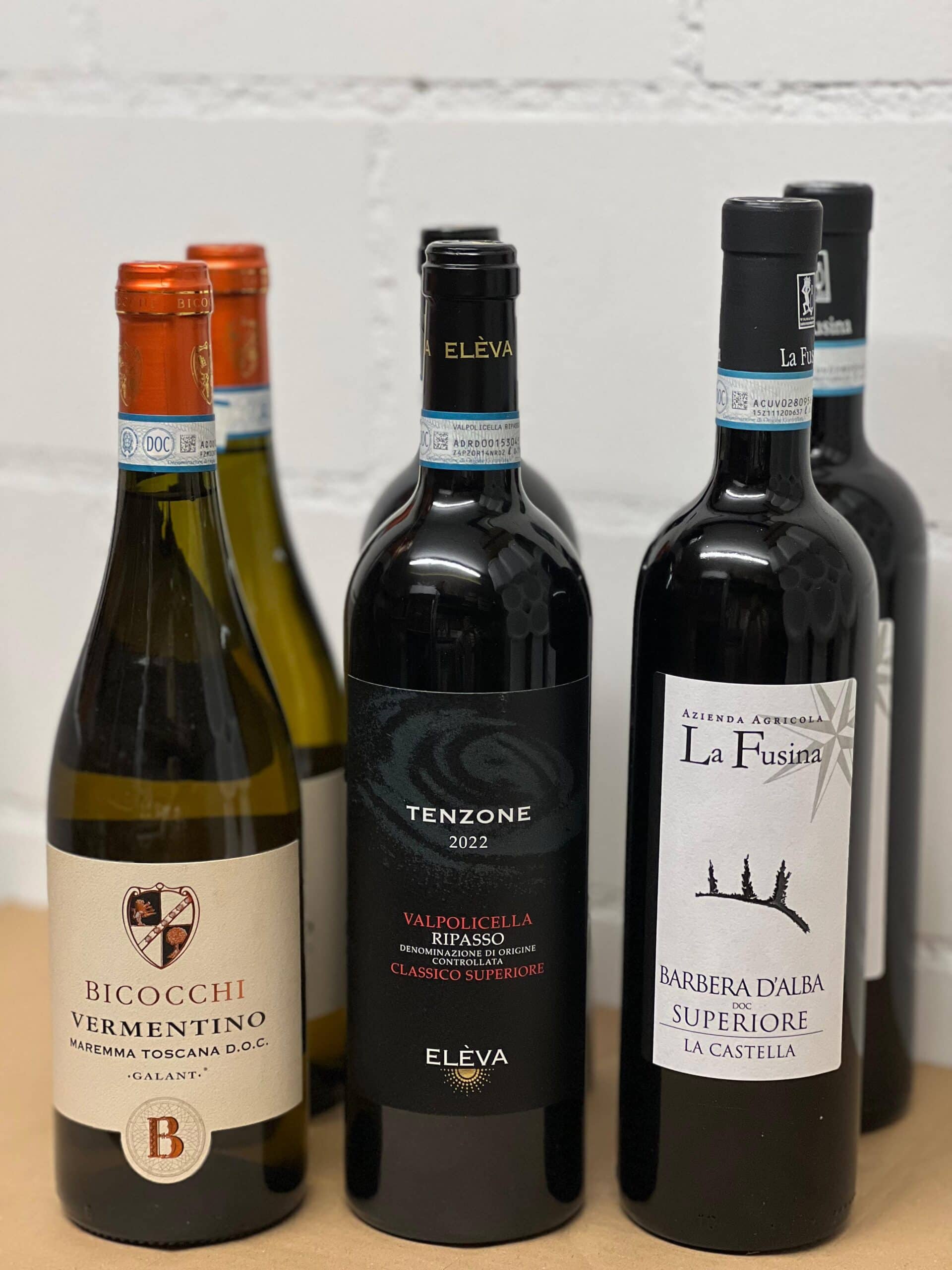 Weinset Italien Sechs Flaschen italienischer Wein nebeneinander, darunter Vermentino Maremma Toscana (Bicocchi), Tenzone Valpolicella Ripasso (Elèva) und Barbera d’Alba Superiore (La Fusina).